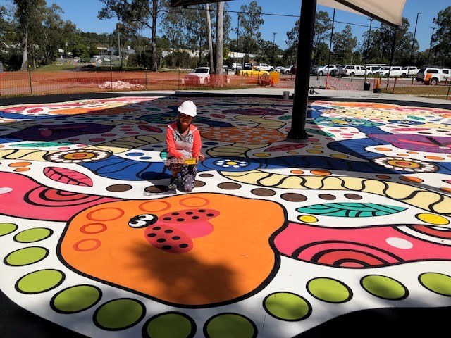 Artist posting on colourful artwork while wearing construction hat