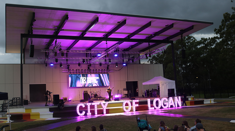 Large stage lit with purple lighting at dusk. Large light up letters read City of Logan