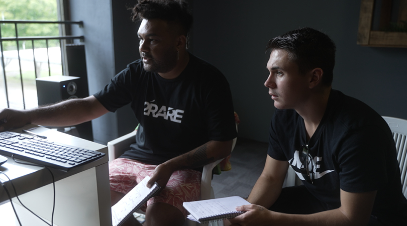 Photo of two men working at a computer with notebooks