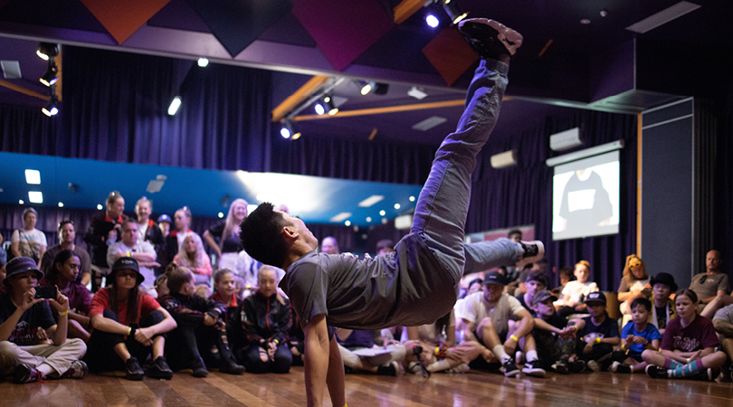 Photo of a man break dancing for an audience including children