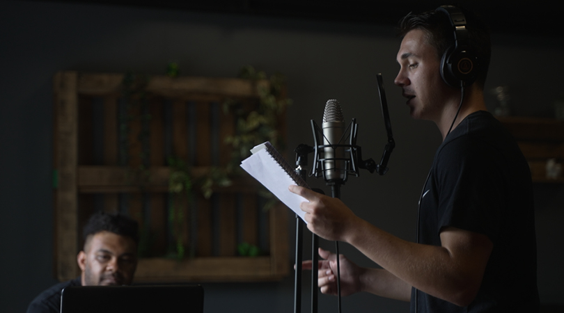 Photo of man singing into microphone with notebook