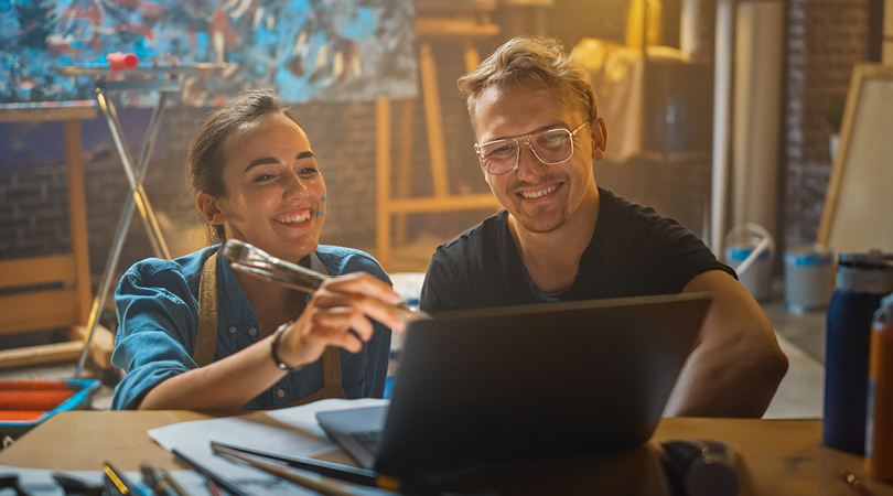 Two people sitting at a laptop computer in an art studio