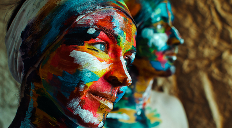 Two people looking into the distance with their faces painted with bright colours