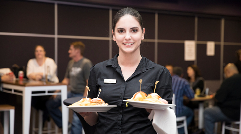 Staff member serving two plates of food in busy venue