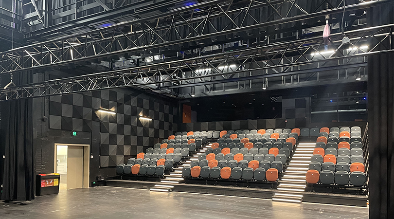 wide angle photo of auditorium seating with metal trusses visible on the ceiling above the stage