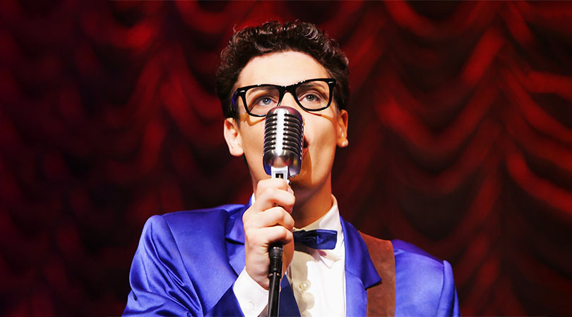 man in blue suit wearing dark sunglasses singing into old style microphone