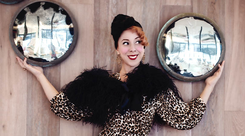 Lady wearing leopard print and black feather neck collar holding two shiny round objects