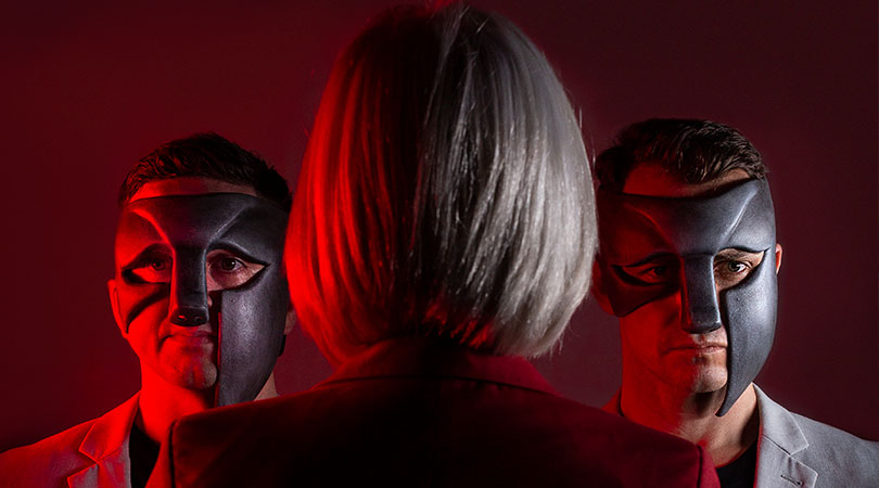 two man in masks facing blonde lady with back to camera