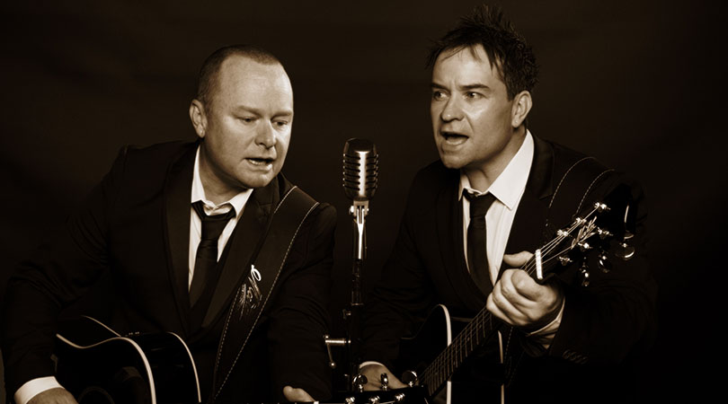two men playing guitar singing into old style microphone in sepia tone