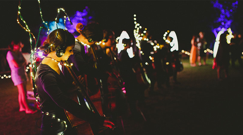 a line of musicians playing instruments at night time with fairy lights attached to them