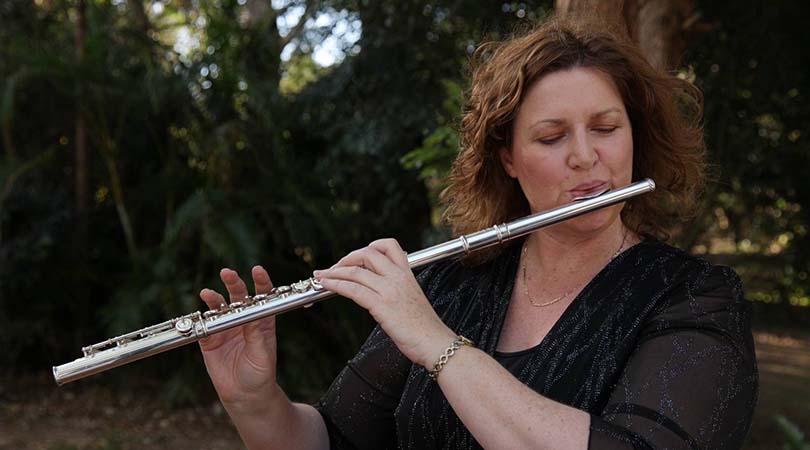 Karen Lonsdale playing the flute outdoors with trees in the background