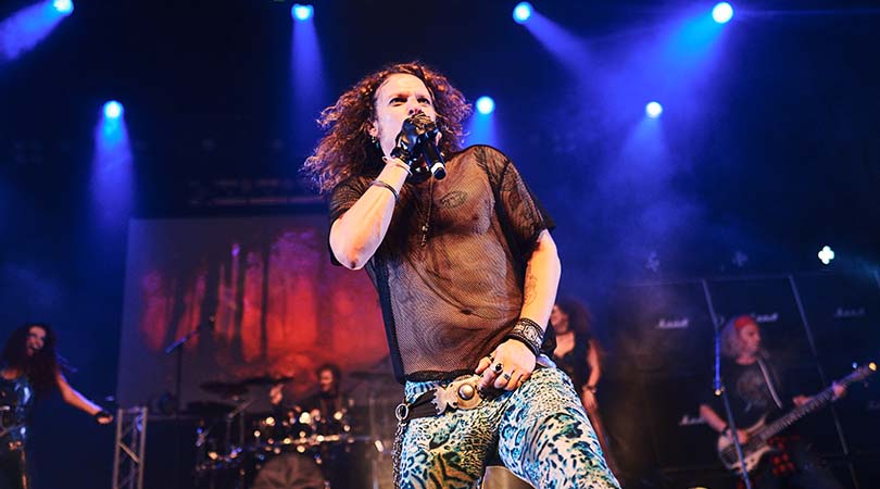 man with long hair on stage singing into microphone
