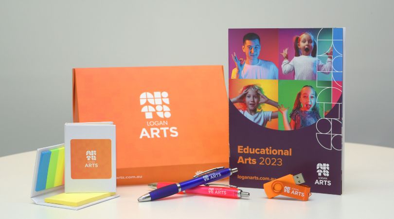 Logan Arts Education Welcome Pack. Orange box with an educational arts booklet, 2 coloured pens, a sticky note pad and a orange USB stick