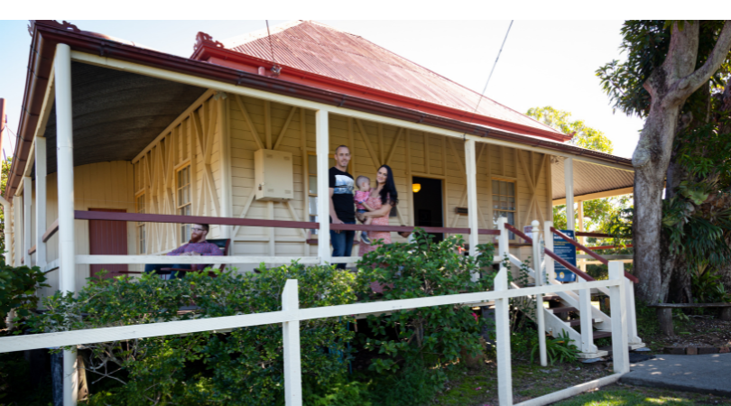 People enjoying Mayes Cottage. A couple hold a baby on the home's balcony