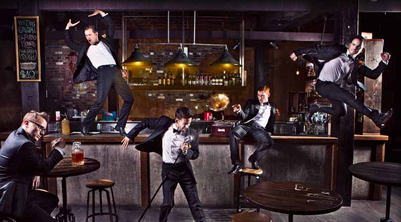5 men in suits in various dance poses around a bar