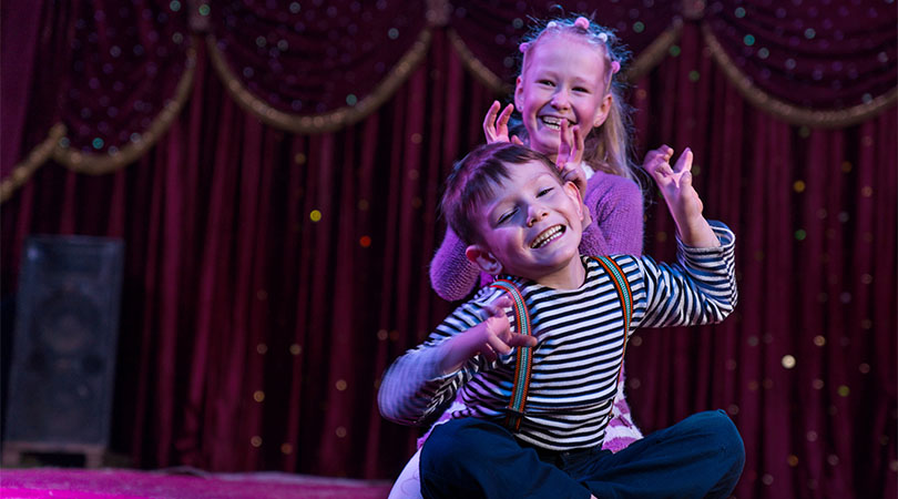 two children pulling funny poses in front of a maroon curtain