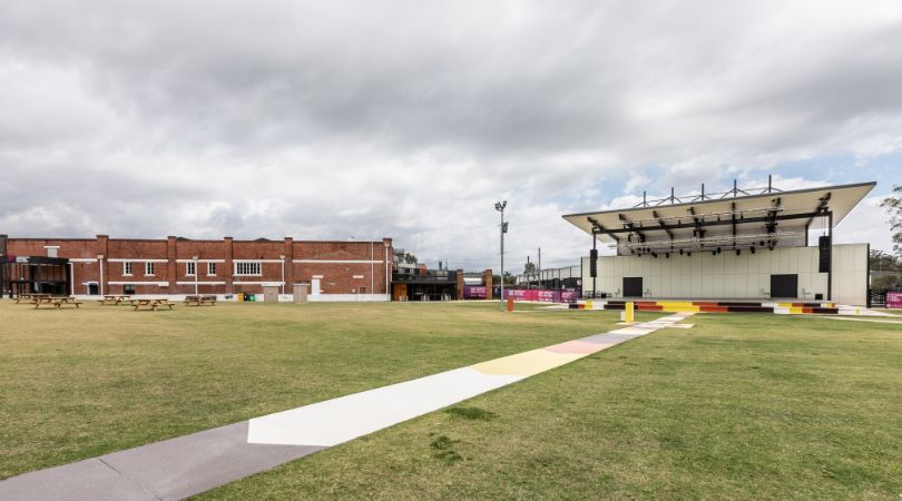 The outside grounds of the Kingston Butter Factory Cultural Precinct including the renovated butter factory building, grassed area, and large performance stage.